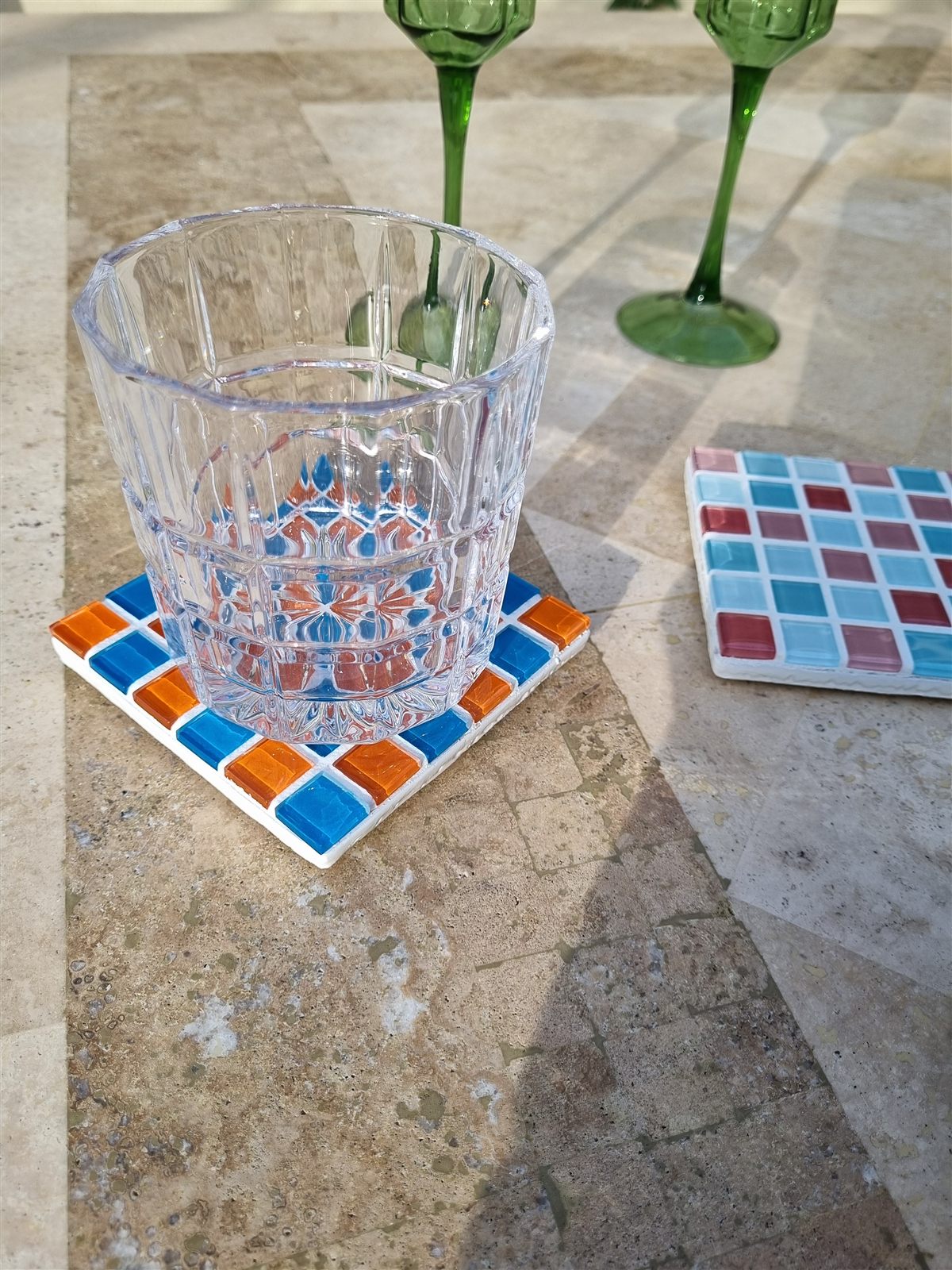 Aperol coaster, bright multicoloured glass tiles on travertine in the sun