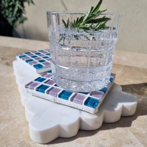 Pigeon Wing handmade glass coaster in teal and lilac grey with a glass of water and rosemary